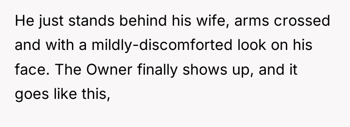 He just stands behind his wife, arms crossed and with...
